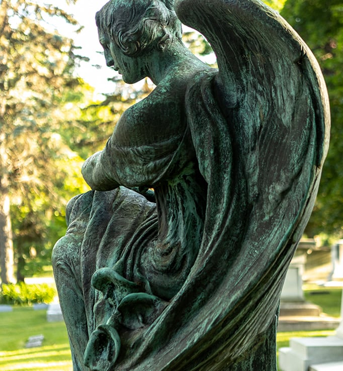 Photo of a guardian angel statue overlooking headstones
